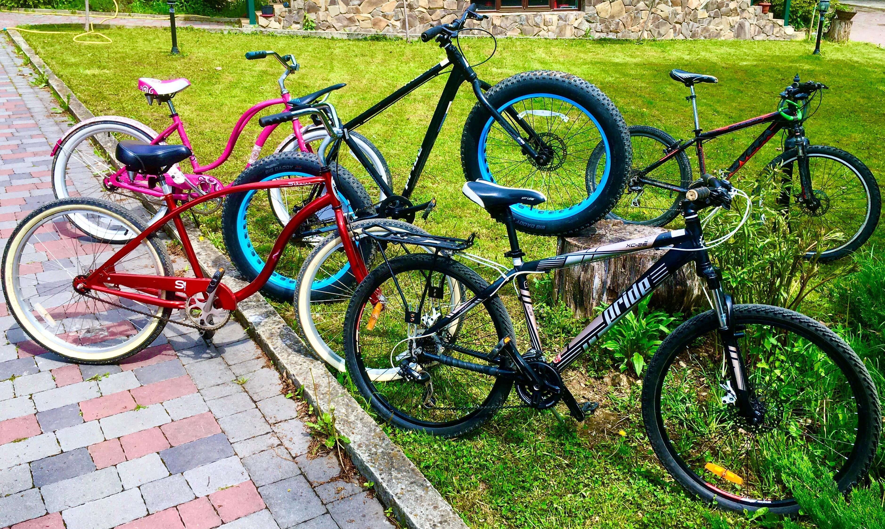Uma fileira de bicicletas estacionadas sobre um caminho de tijolos, ao lado de uma área gramada.