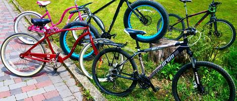 Uma fileira de bicicletas estacionadas sobre um caminho de tijolos, ao lado de uma área gramada.