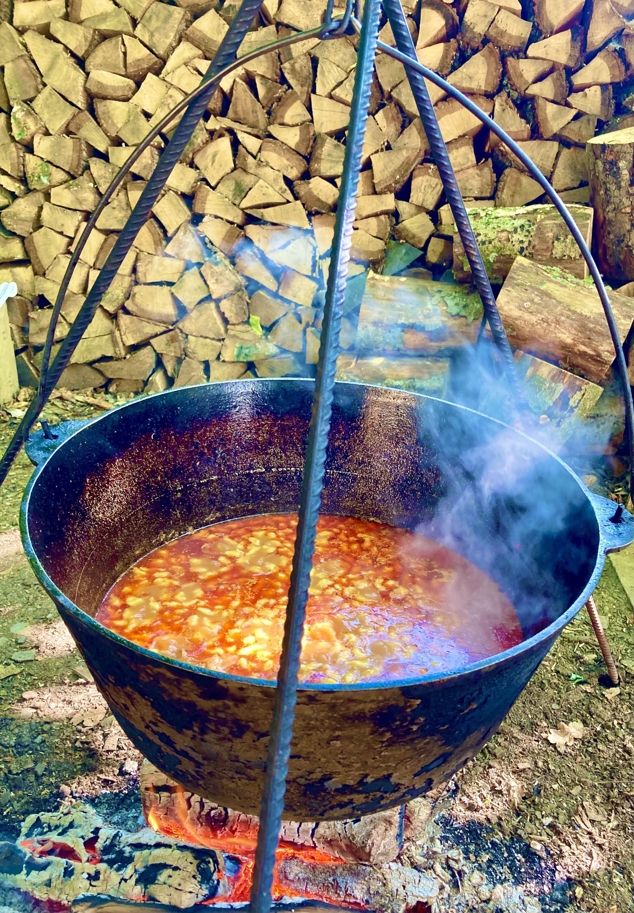 Una olla de metal grande sobre fuego abierto, con vapor saliendo de su interior.