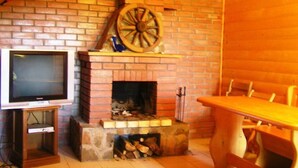 Ein gemütliches Zimmer mit Kamin aus Backsteinen, einem Fernseher auf einem Holzboden und einem Holztisch.