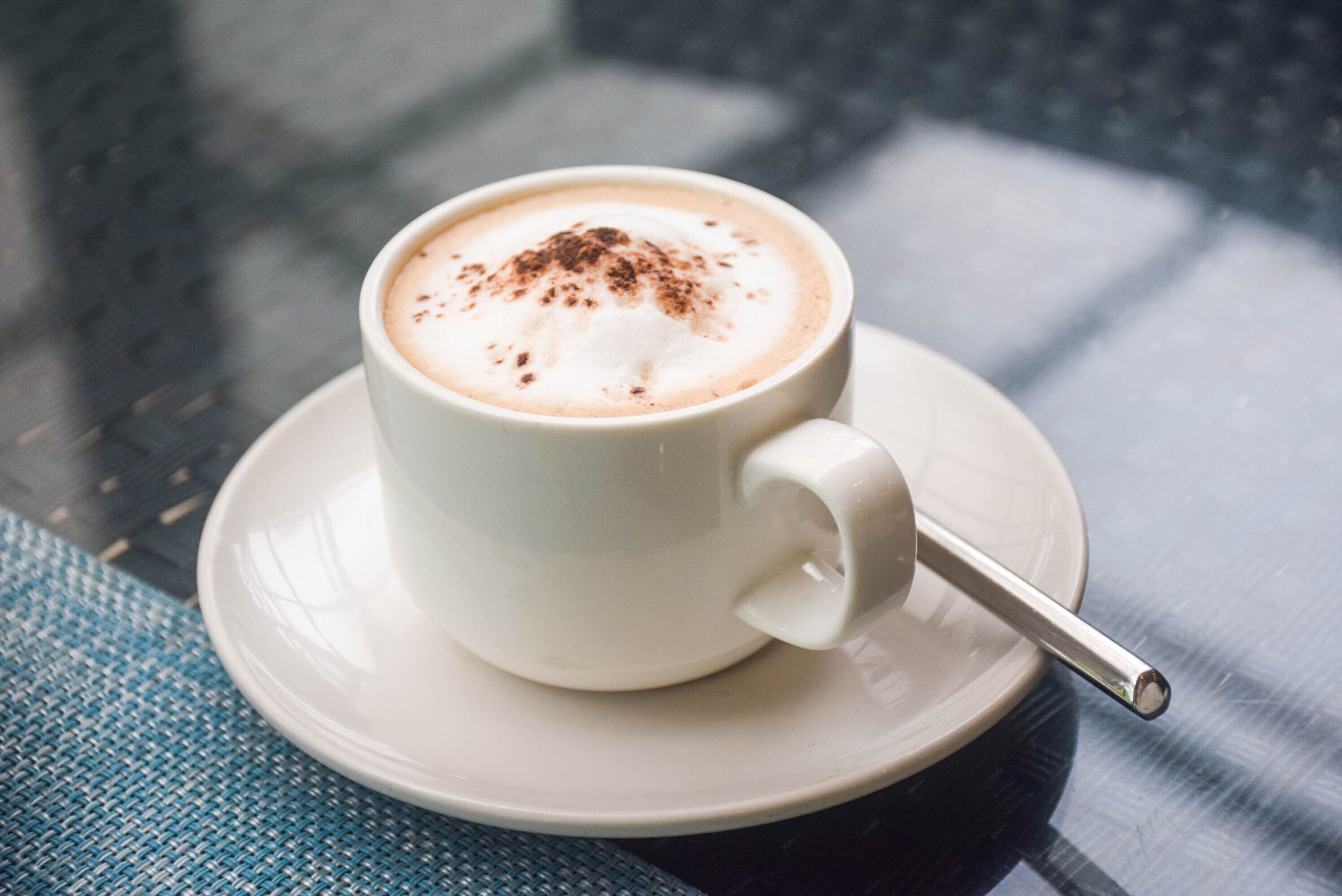 A white cup of coffee with a spoon, placed on a saucer.
