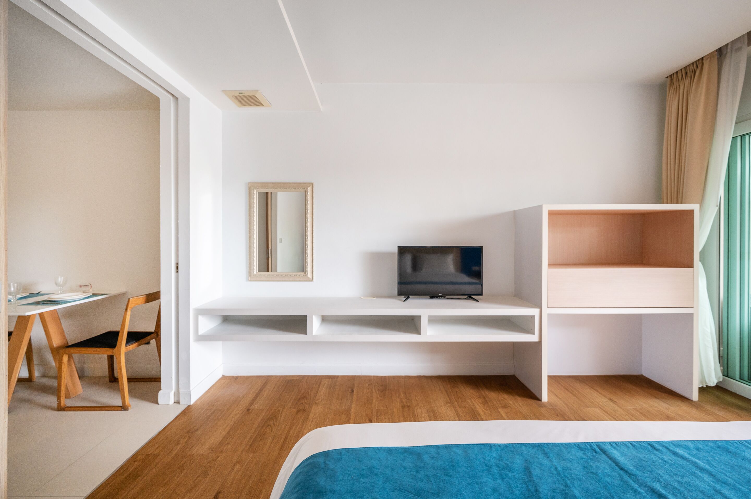 A modern hotel room with a bed, a desk with a TV, a chair, and a small dining table.