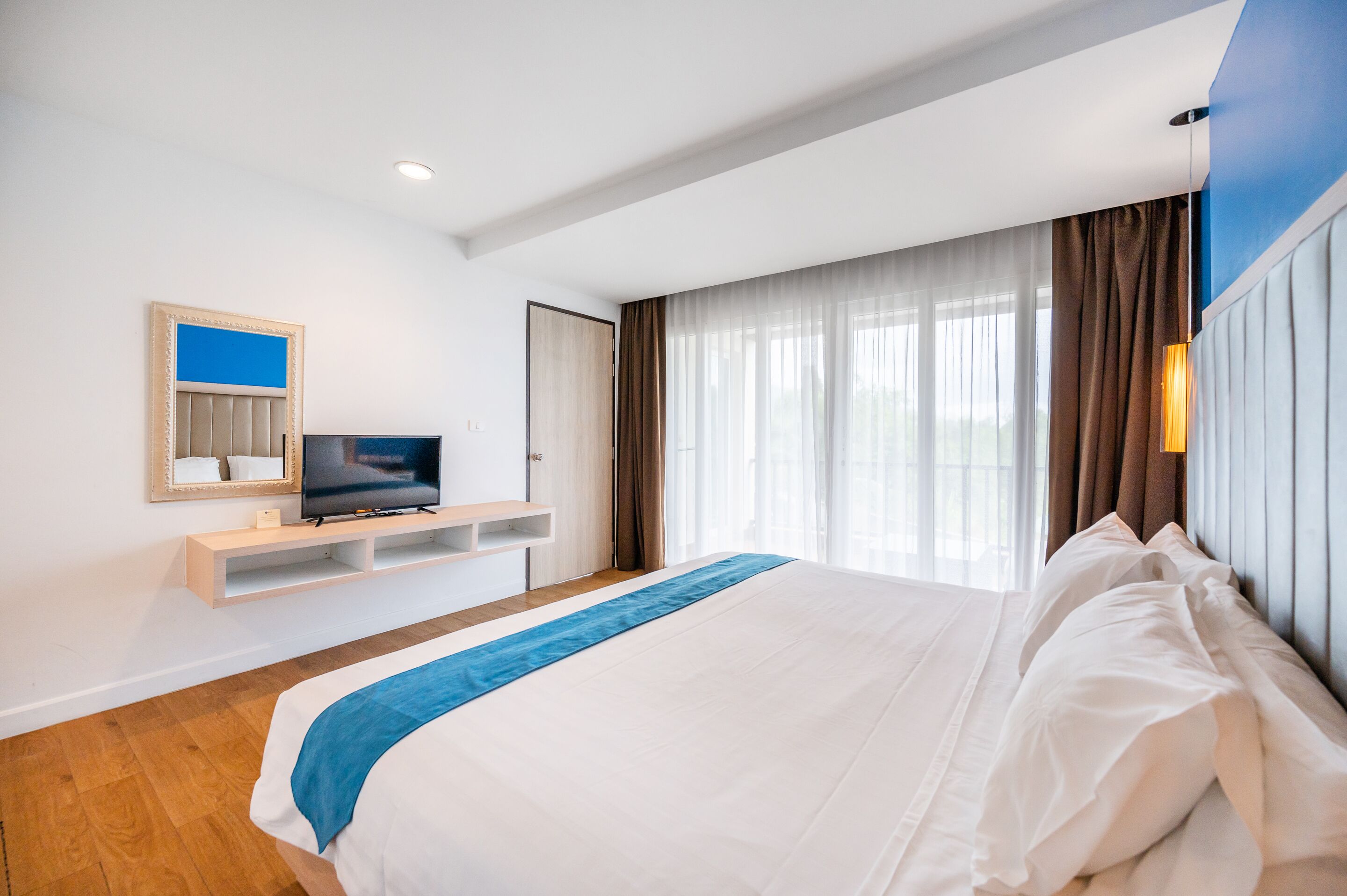 Un cuarto de hotel moderno con una cama grande, un televisor sobre un mueble de madera y vistas al exterior a través de amplios ventanales.