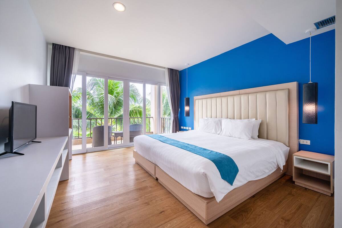 Una habitación de hotel moderna con una cama grande, un televisor y un balcón con vistas a palmeras.