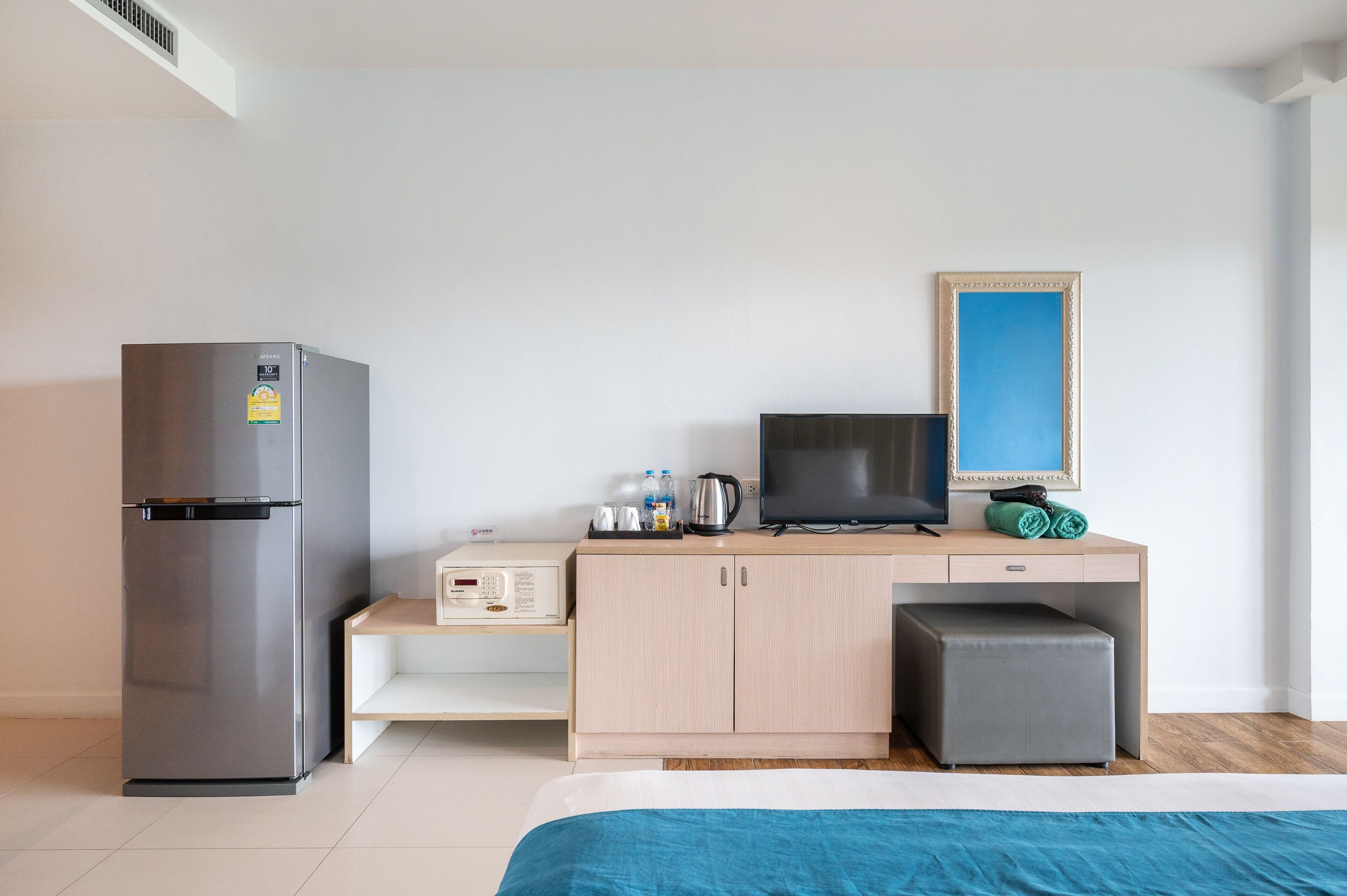 Una habitación de hotel con cama, escritorio con computadora, televisión, refrigerador y un mueble pequeño.