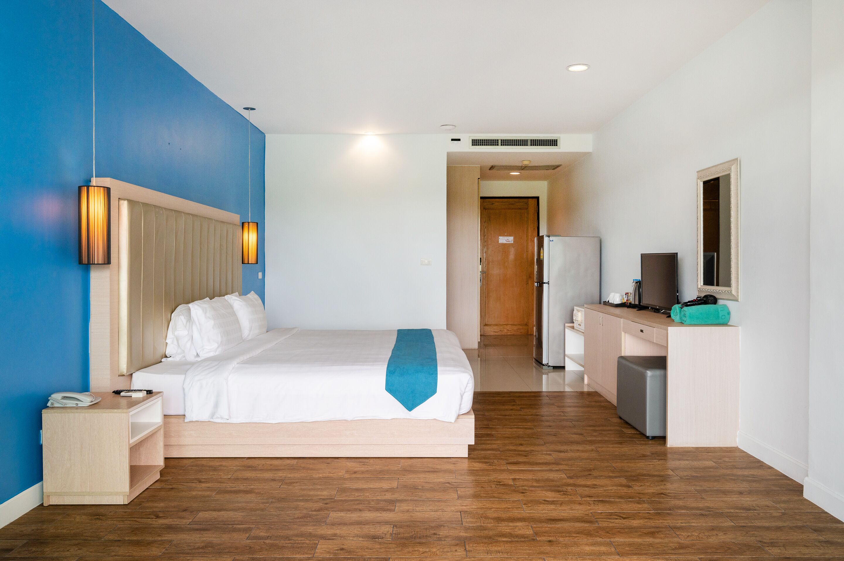 A hotel room with a bed, bedside table, and a kitchenette area.