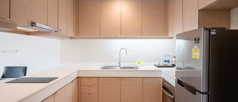 A modern kitchen with wooden cabinets, a stainless steel refrigerator, and a white countertop.
