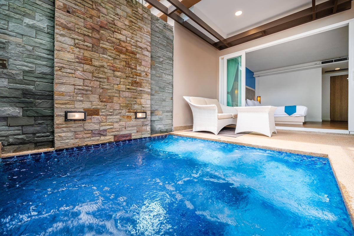 Una piscina con paredes de piedra, una silla blanca y una cama al fondo.