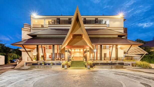 Un hotel moderno con una entrada triangular destacada, varios balcones y una fachada bien iluminada.