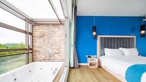Una habitación de hotel moderna con un ventanal grande, una pared de piedra, una pared azul de acento, una cama, una mesita de noche y una bañera.