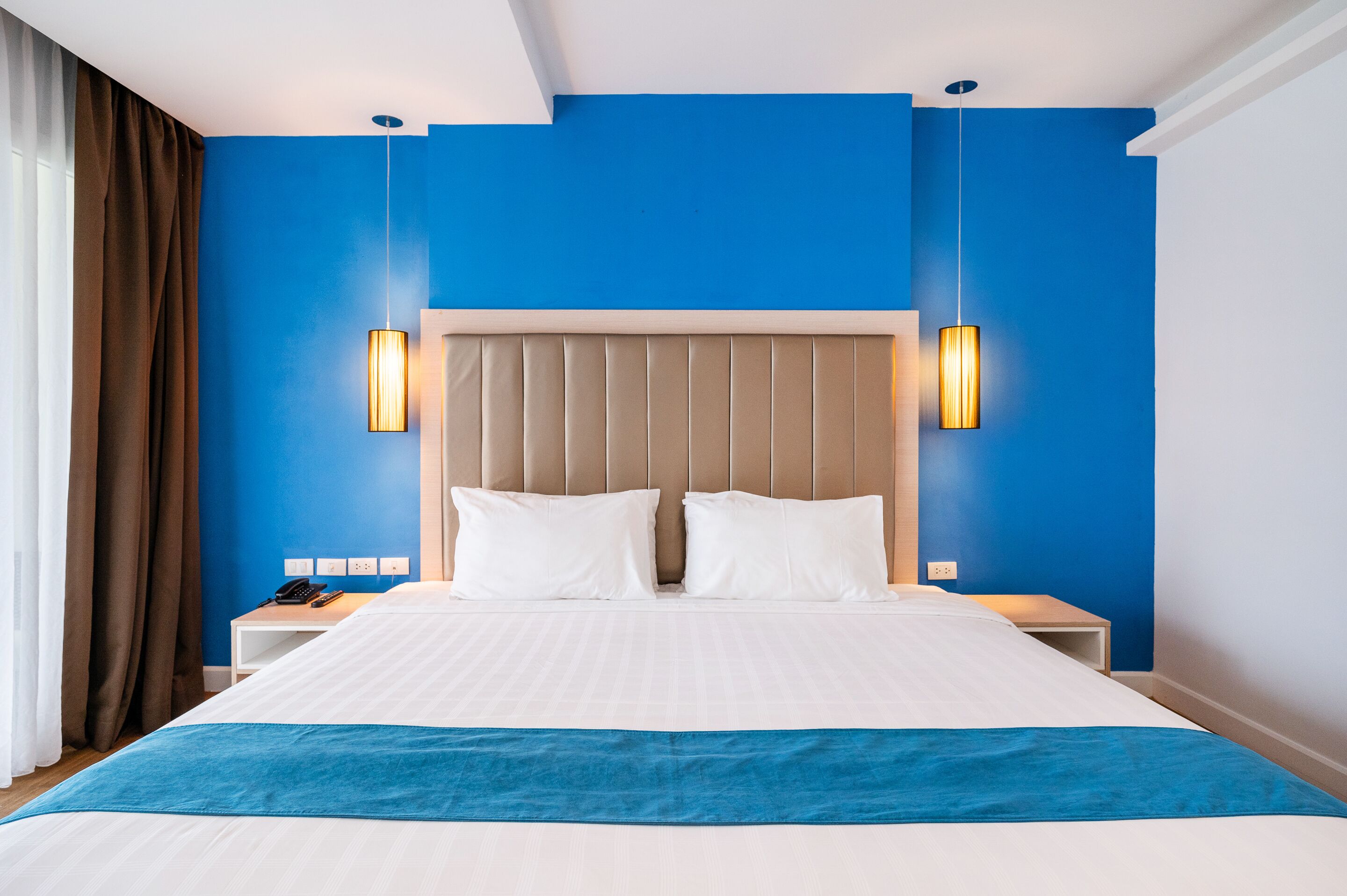 A hotel room with a large bed, two bedside tables, a headboard, and a blue accent wall.