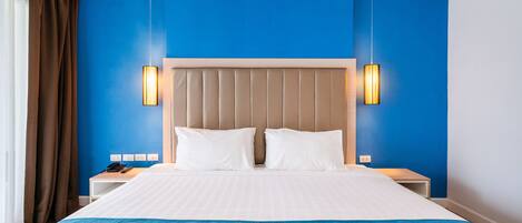 A hotel room with a large bed, two bedside tables, a headboard, and a blue accent wall.