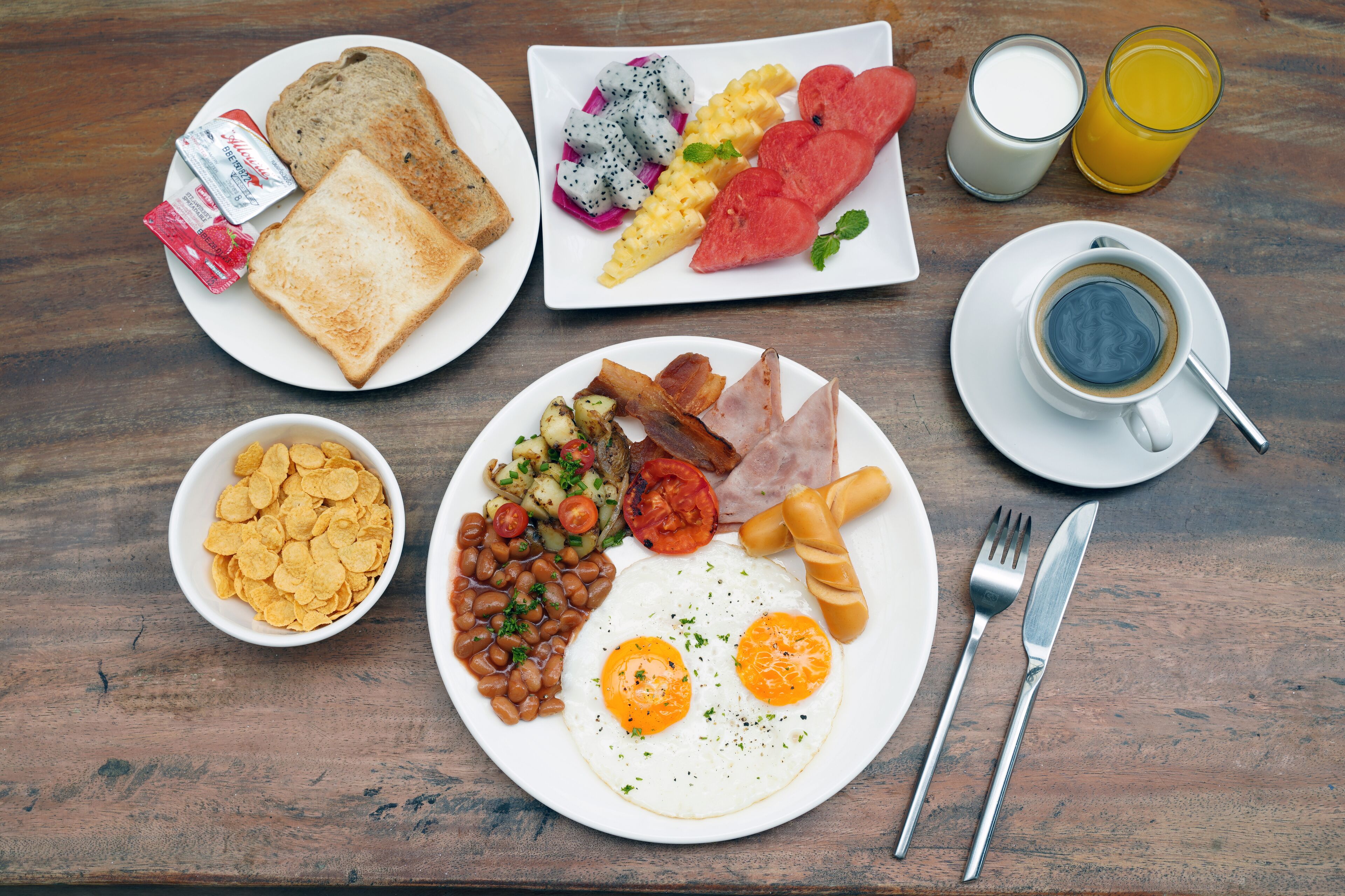 Un copieux petit-déjeuner composé de pain grillé, d’œufs, de bacon, de haricots, ainsi qu’une variété de fruits et de légumes, le tout disposé sur une table en bois.