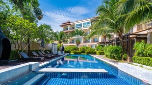 Una piscina con borde de baldosas, rodeada de palmeras y sillones de descanso.
