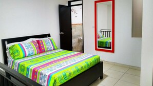 Una cama con ropa de cama colorida, un cabecero negro y un espejo con marco rojo en la pared.