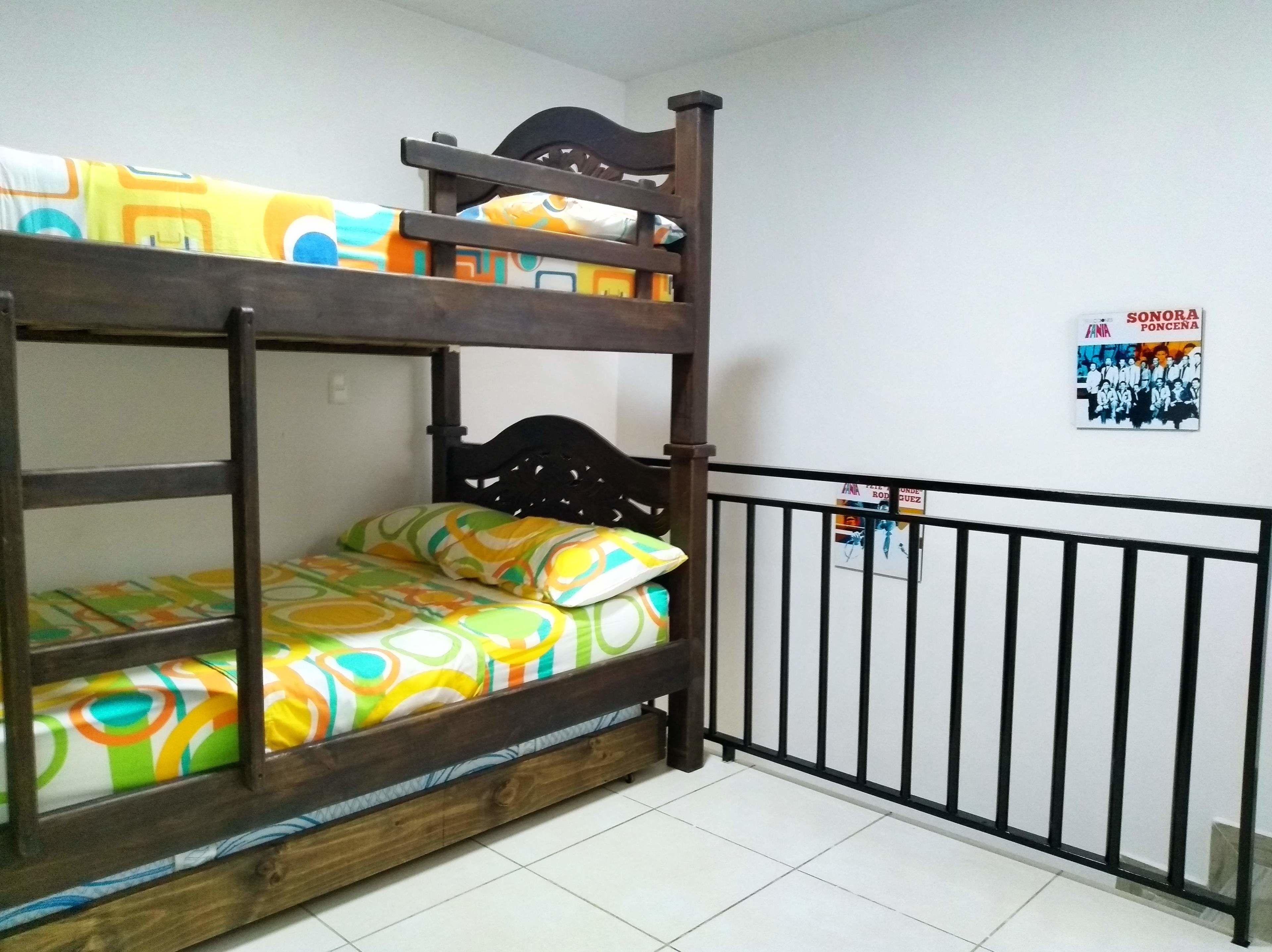 Una cama individual con ropa de cama colorida en una habitación con paredes blancas y suelo de baldosas.