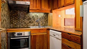 A compact kitchen with wooden cabinets, a stainless steel oven, a dishwasher, and a stone backsplash. - 3-room apartment near the slopes - Courchevel 1850 (Courchevel 1850)