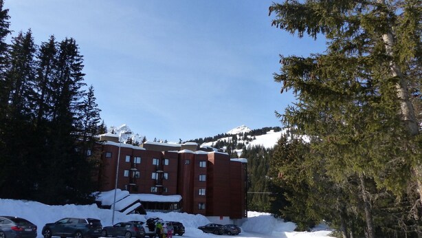 A multi-story building with a red facade, surrounded by snow-covered ground and trees. - 3-room apartment near the slopes - Courchevel 1850 (Courchevel 1850)