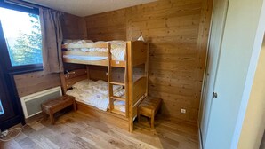 A room with wooden bunk beds, a small wooden bench, and a window with curtains. - 3-room apartment near the slopes - Courchevel 1850 (Courchevel 1850)