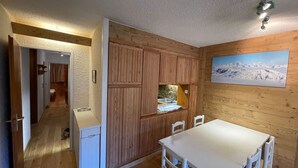 A wooden interior with a dining area, a kitchen with wooden cabinets, and a view of a snowy mountain. - 3-room apartment near the slopes - Courchevel 1850 (Courchevel 1850)