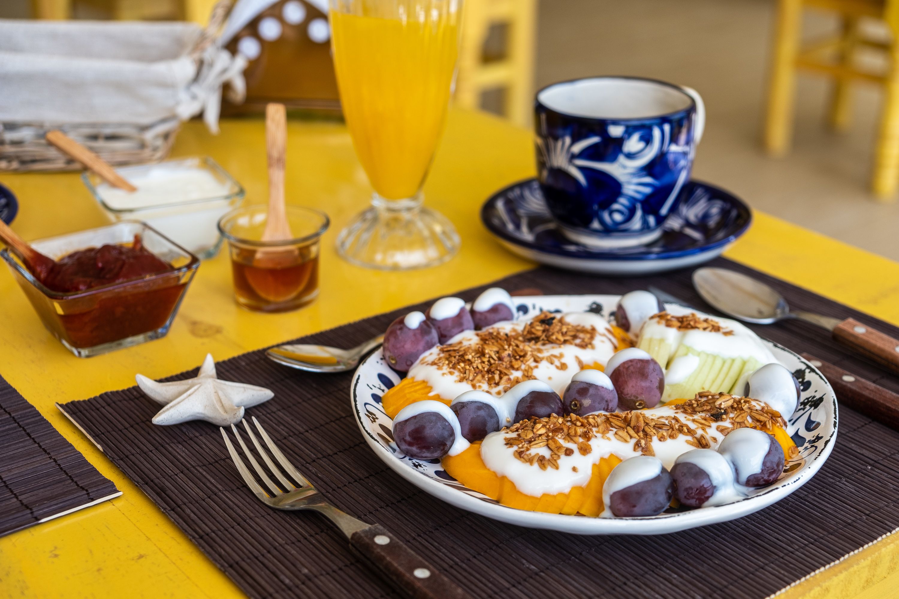 Un desayuno con un plato de comida, una taza de café y un vaso de jugo de naranja sobre una mesa amarilla.