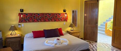 A hotel room with a bed, two nightstands, a wall tapestry, and a wooden door.