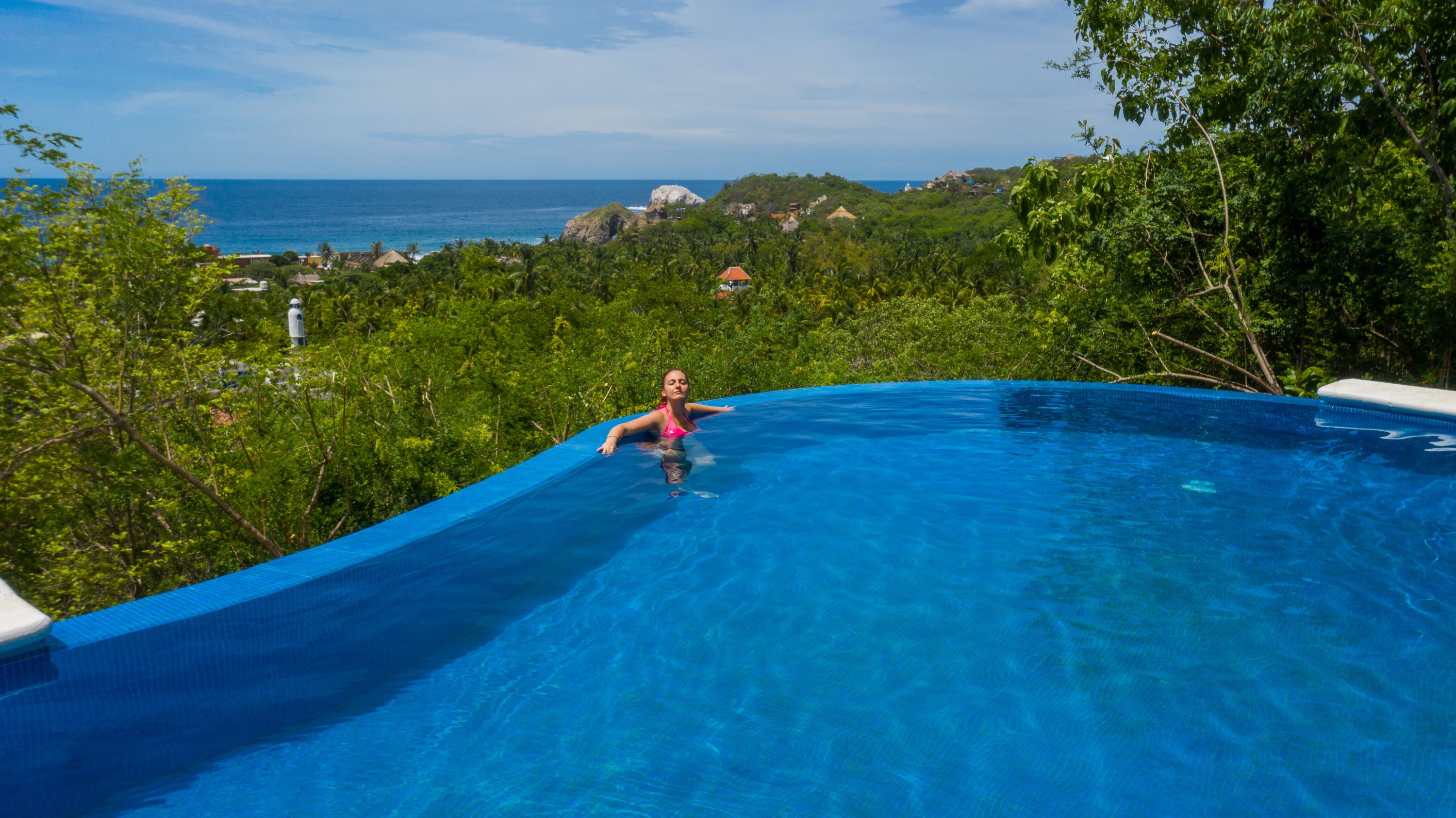 Una persona en una piscina con vistas al océano y abundante vegetación.