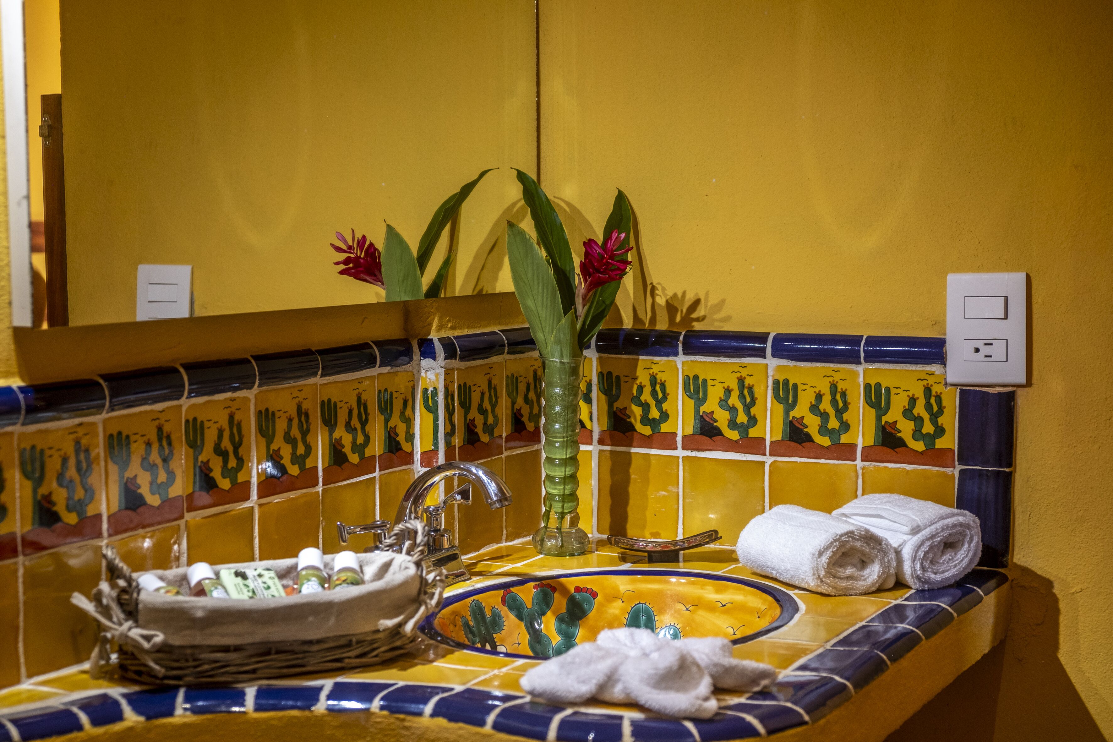 A bathroom with a yellow tiled backsplash, a sink with a glass vase, and a mirror.