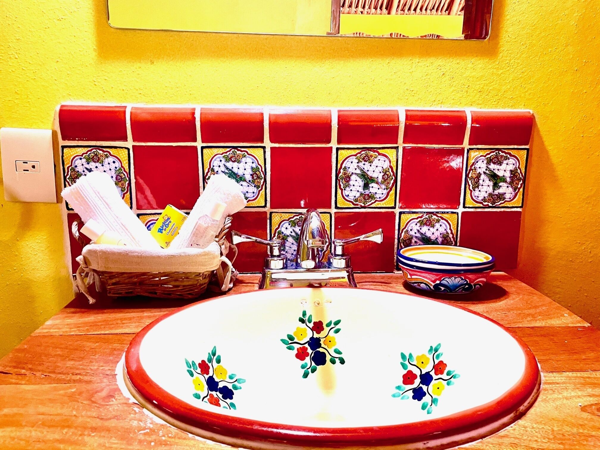 A bathroom with a sink, a basket of toiletries, and a decorative tile backsplash.