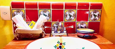 A bathroom with a sink, a basket of toiletries, and a decorative tile backsplash.