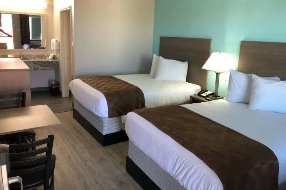 Quarto de hotel com duas camas, uma mesa de trabalho e banheiro.