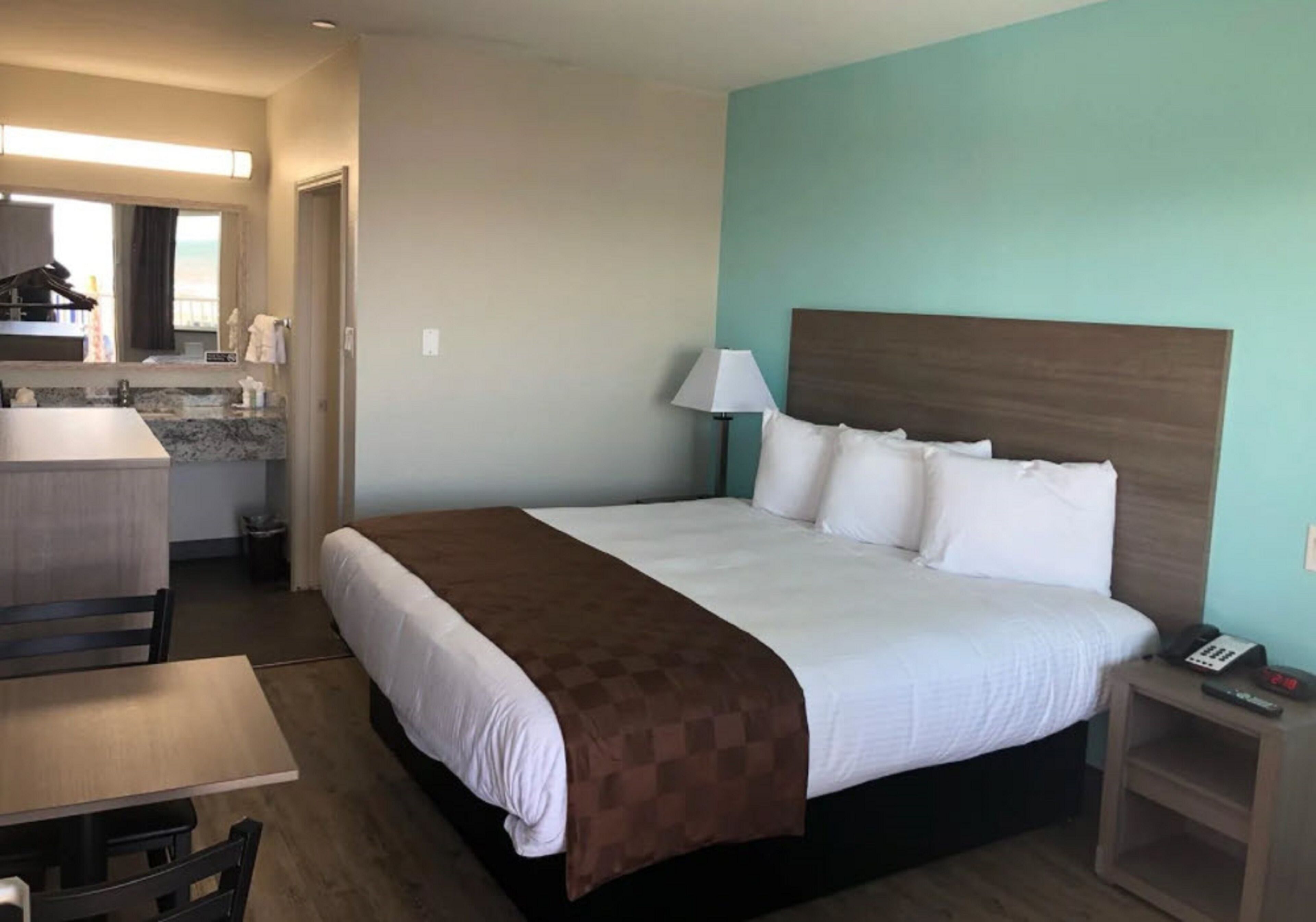 Une chambre d’hôtel avec un lit, un bureau, une chaise, une lampe et une petite table.