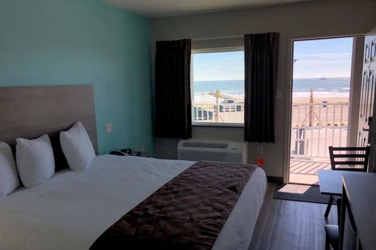 Quarto de hotel com cama, escrivaninha e vista para a praia.