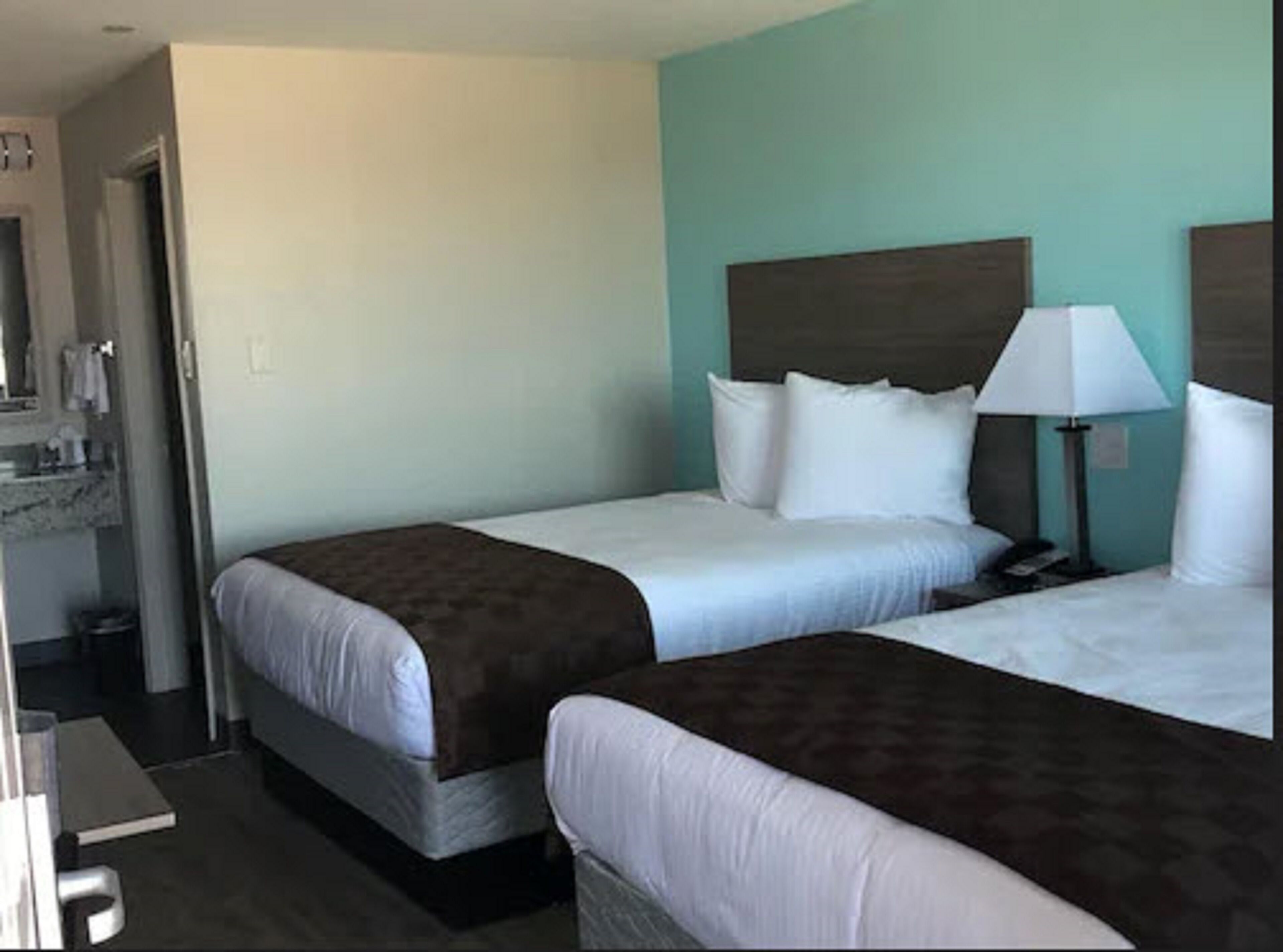 A hotel room with two beds, a nightstand, a lamp, and a bathroom visible through an open door.