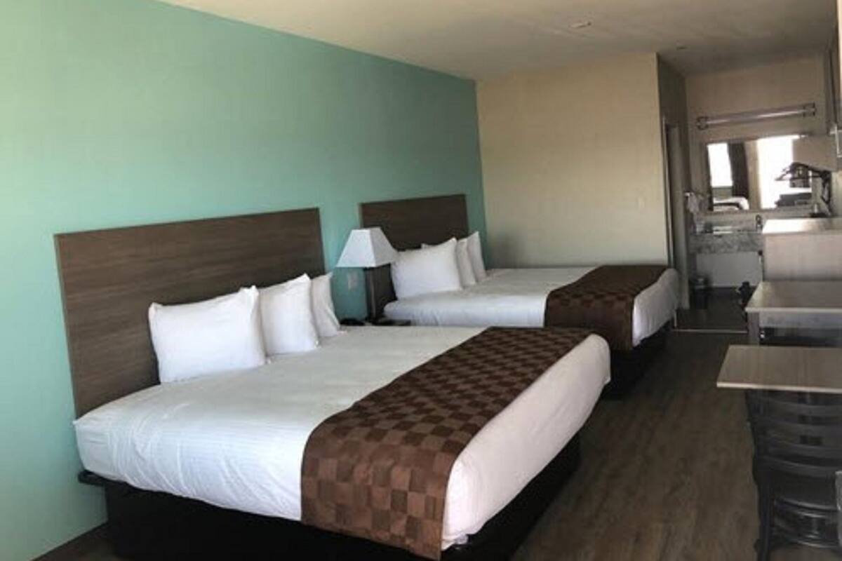 Quarto de hotel com duas camas, uma escrivaninha e uma cozinha compacta.