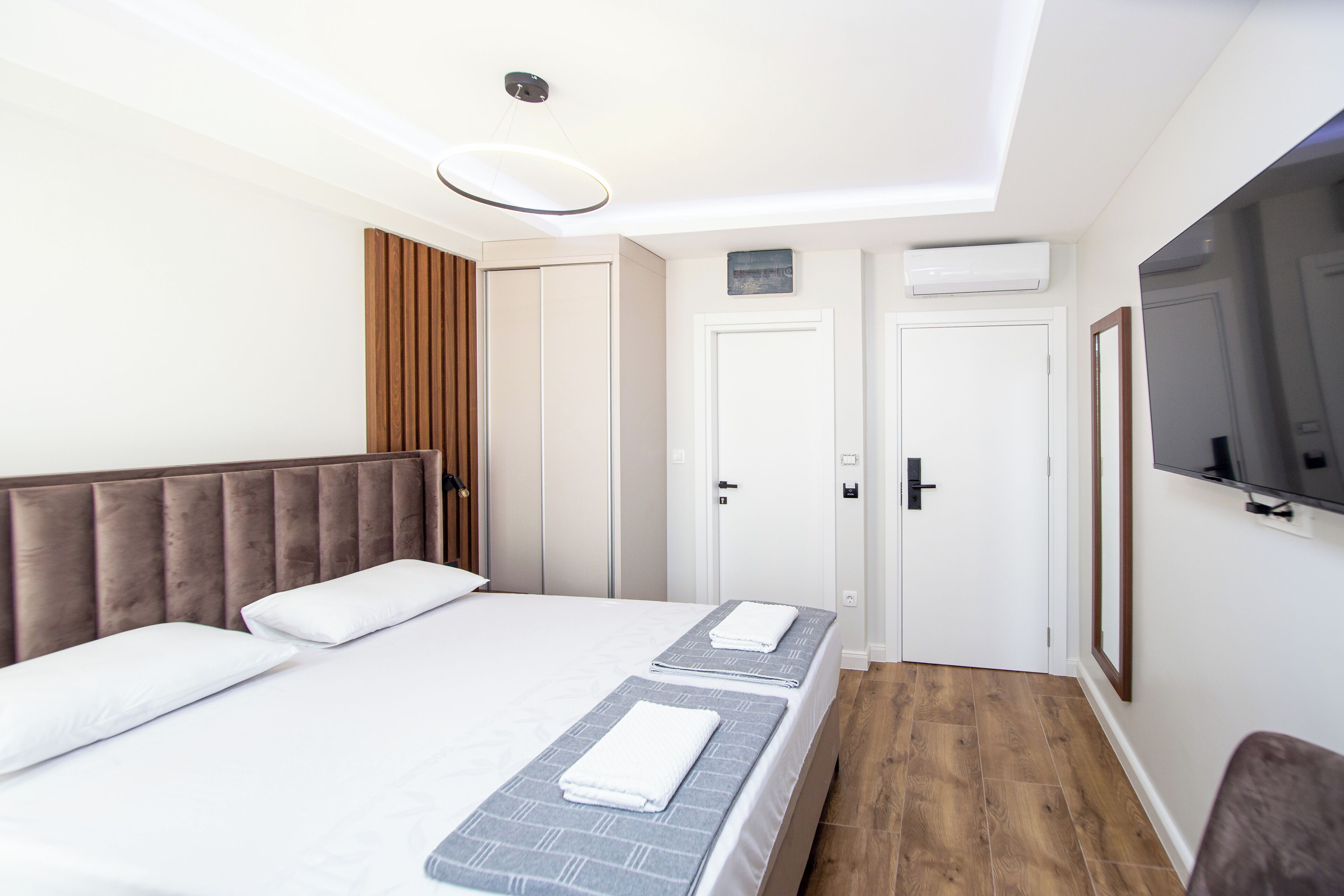 A hotel room with a bed, a bedside table, a mirror, a wardrobe, and an air conditioning unit.