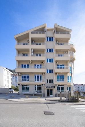 Un hotel de varios pisos con balcones, una entrada principal y un cielo despejado.