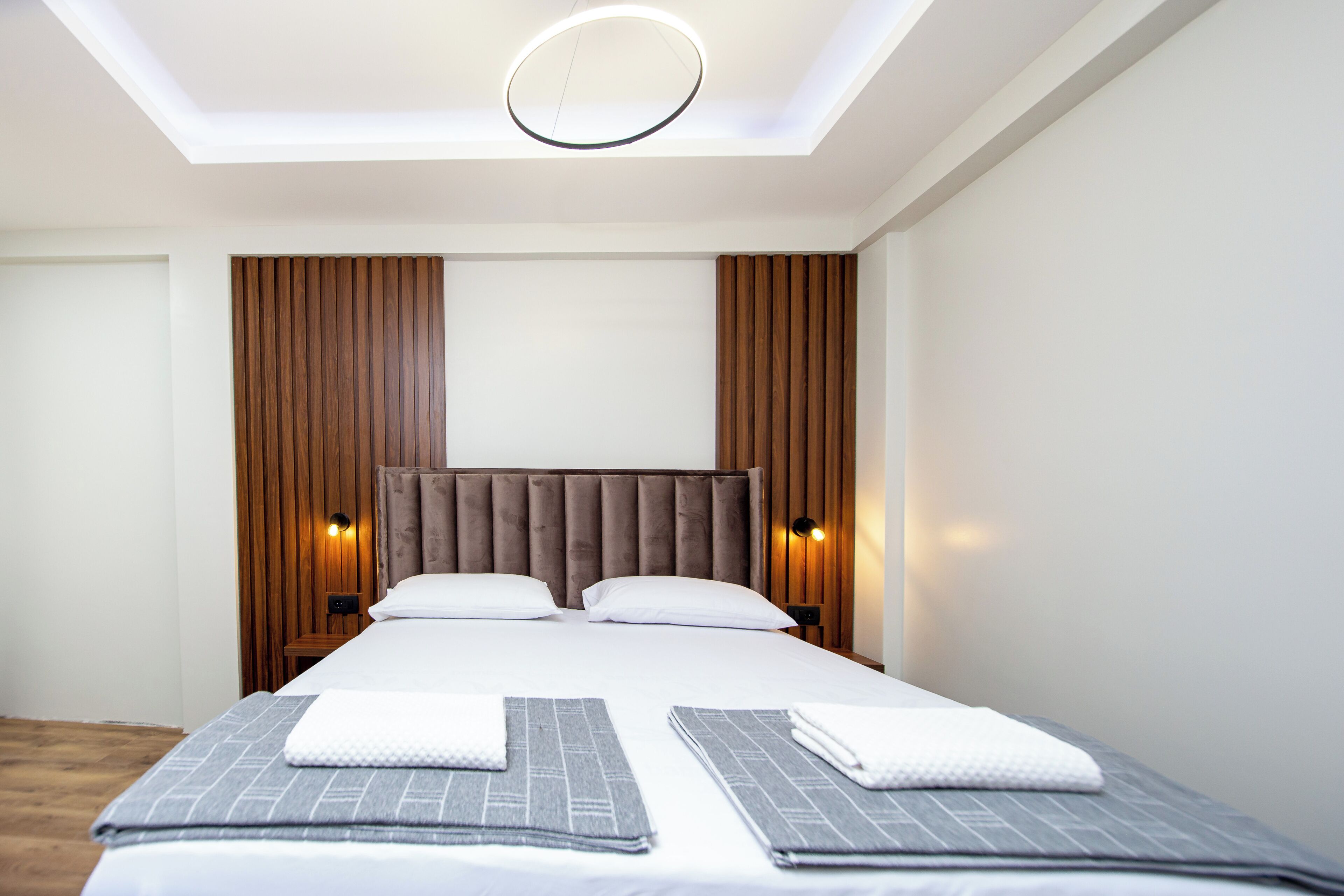A modern hotel room with a large bed, wooden panel walls, and a skylight.