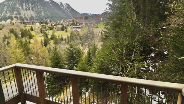 Un balcó amb vista a un paisatge de muntanyes, un poble i una àrea forestal densa.