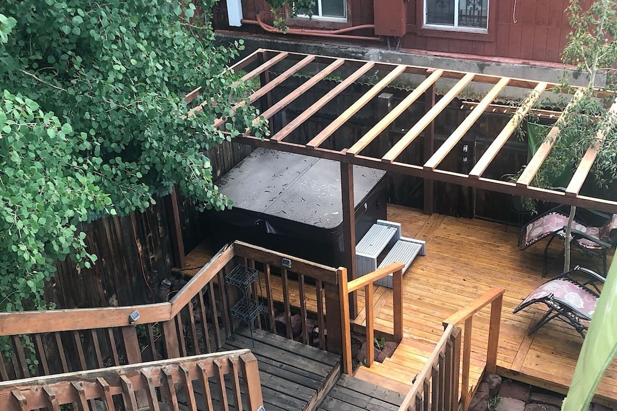 A wooden deck with a barbecue grill, seating area, and a staircase leading to a covered patio.