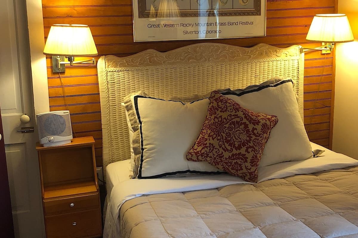 A hotel room with a bed, two bedside lamps, a heater, and a framed picture on the wall.