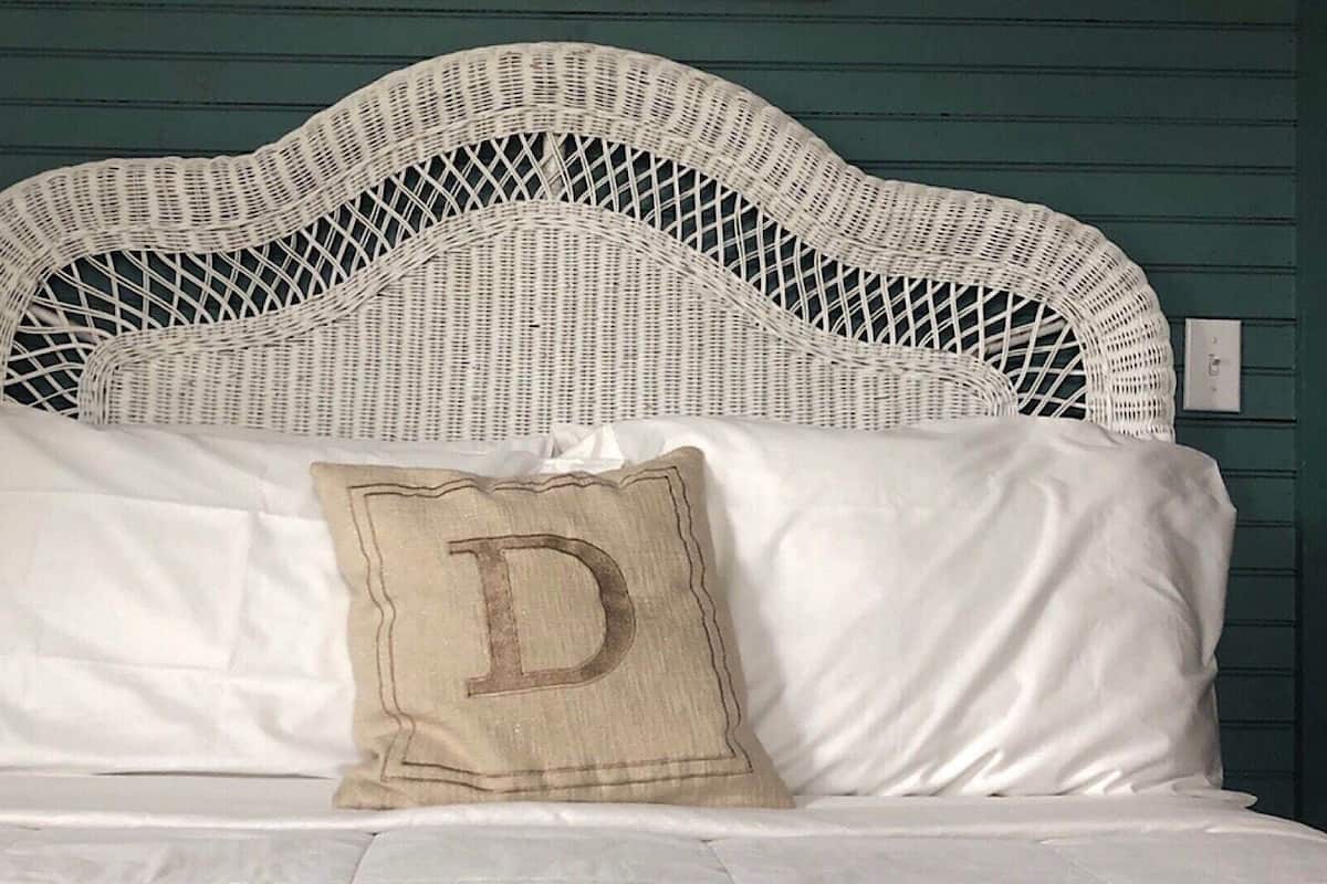 A bed with a white headboard and a pillow with a large letter 'D'.