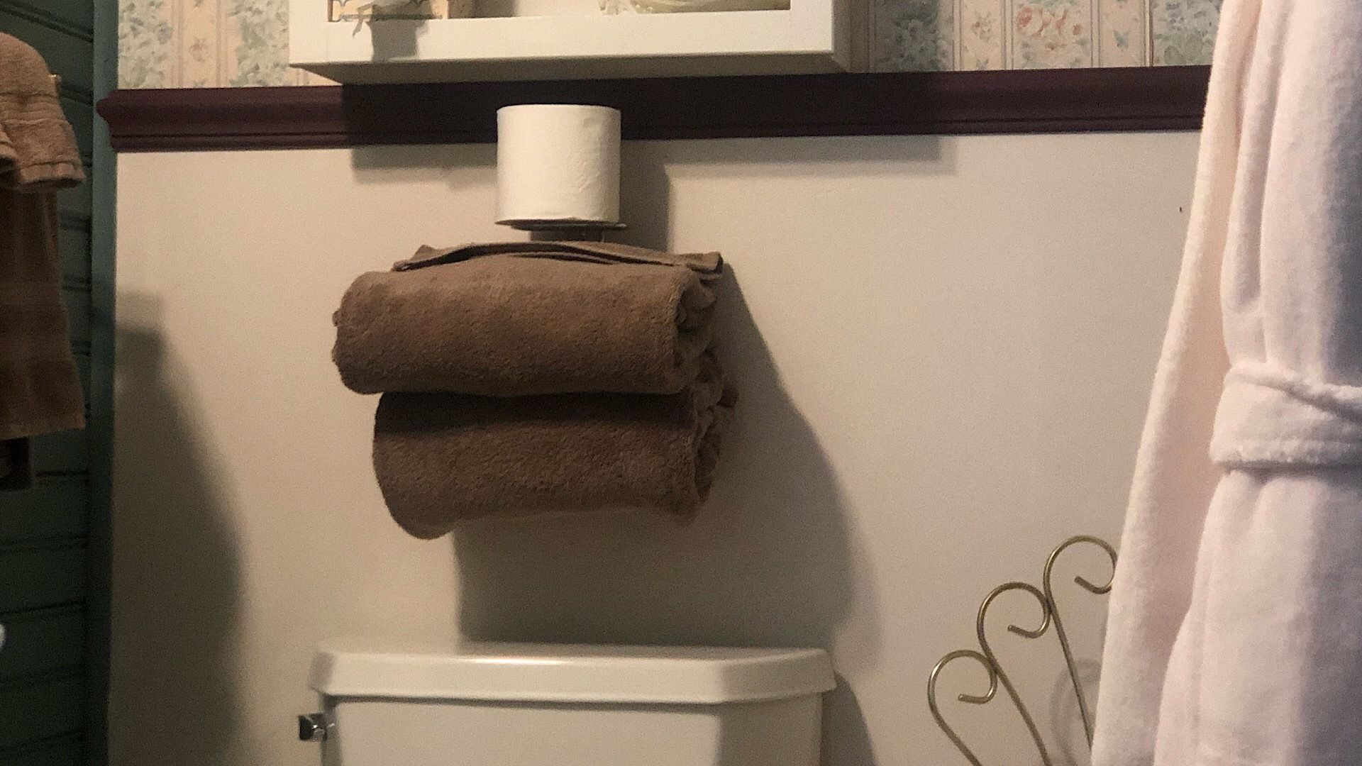 Ein Badezimmer mit Toilette, Handtuchhalter mit gefalteten Handtüchern und Toilettenpapierhalter.