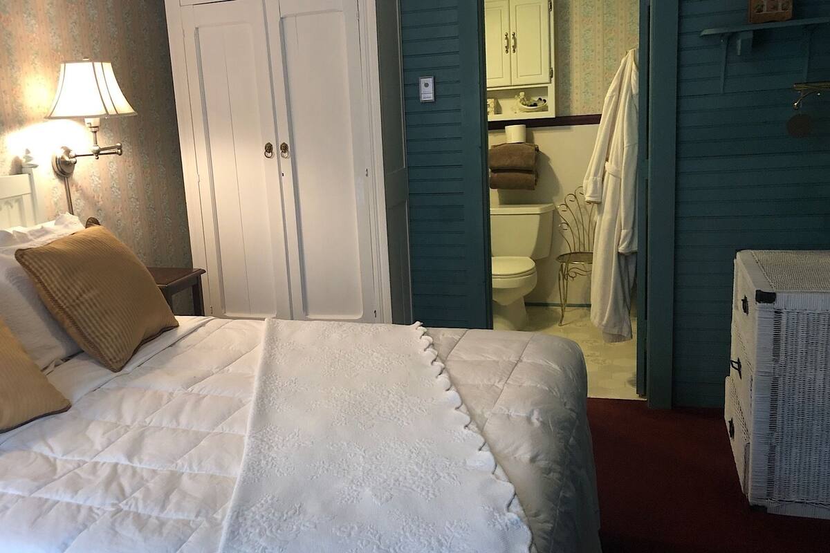 A bedroom with a bed, a nightstand, a lamp, and a view into the bathroom.