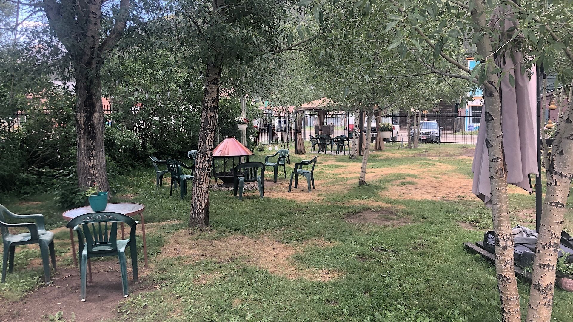 A grassy outdoor area with several green plastic chairs and a small table, surrounded by trees.