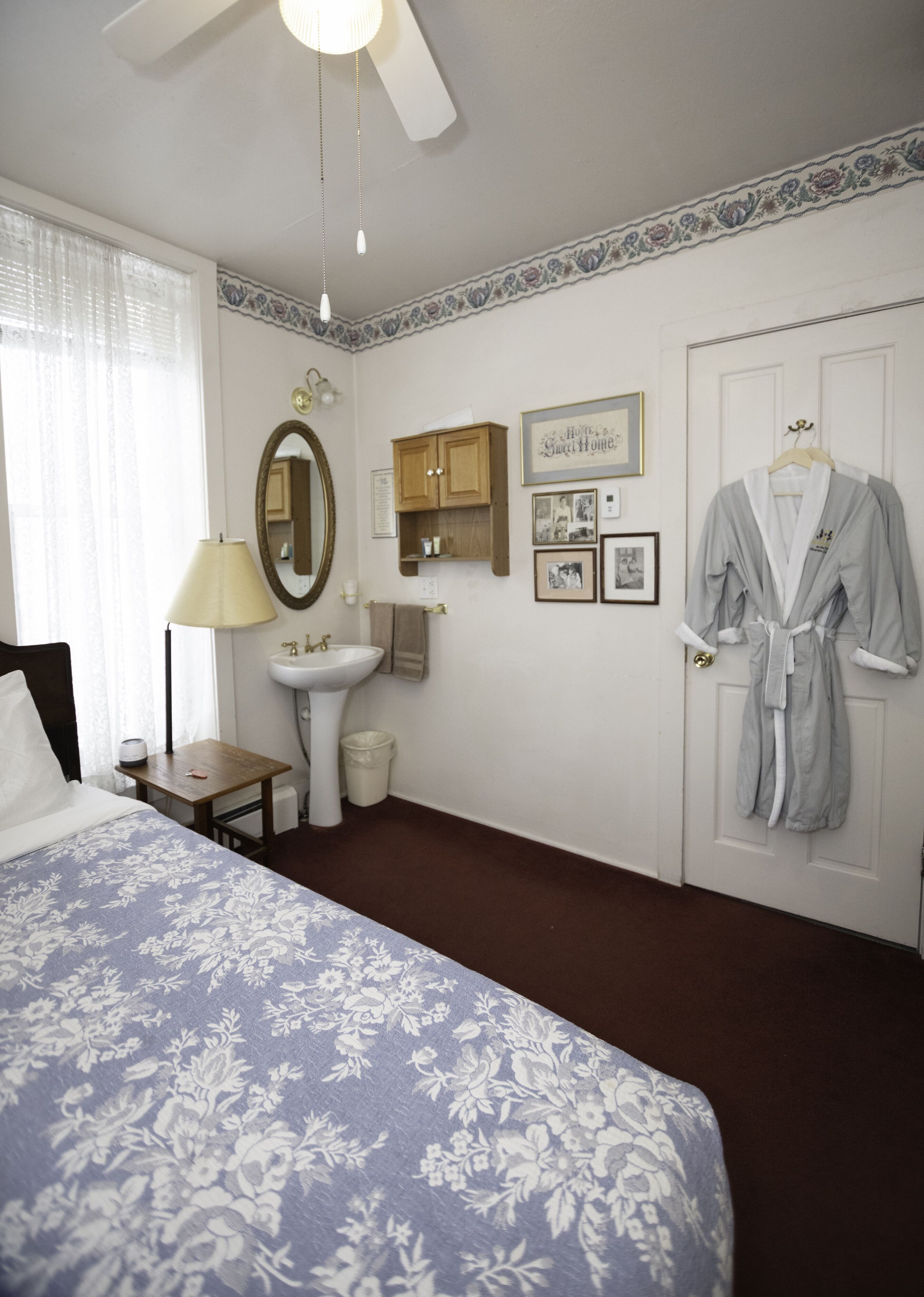 A hotel room with a bed, a bedside table, a lamp, a mirror, a sink, and a robe hanging on the door.