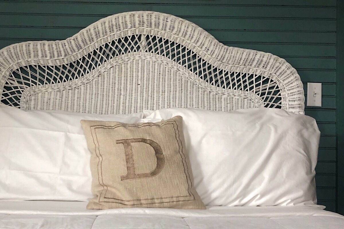 A bed with a white headboard and a pillow with a large letter 'D'.