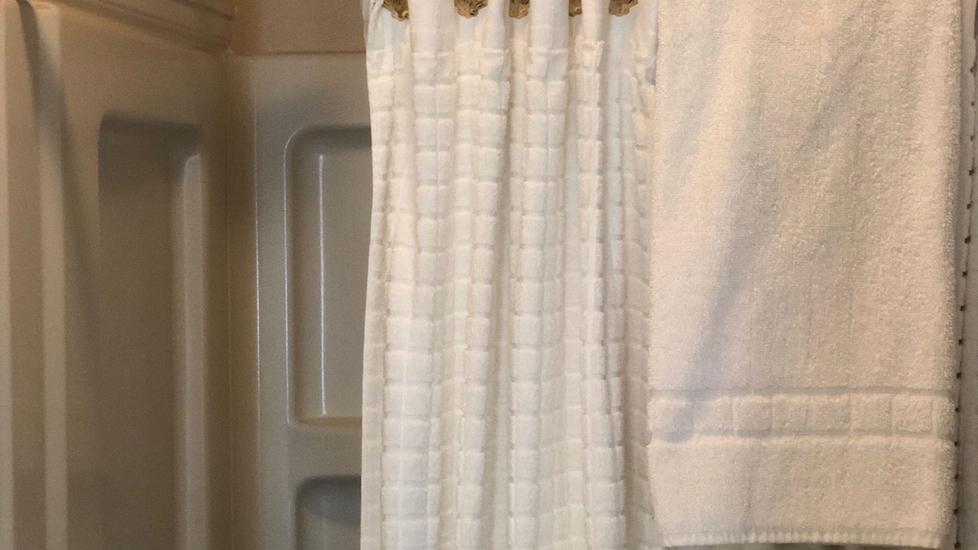 A bathroom with a white shower curtain and a white towel hanging on the wall.