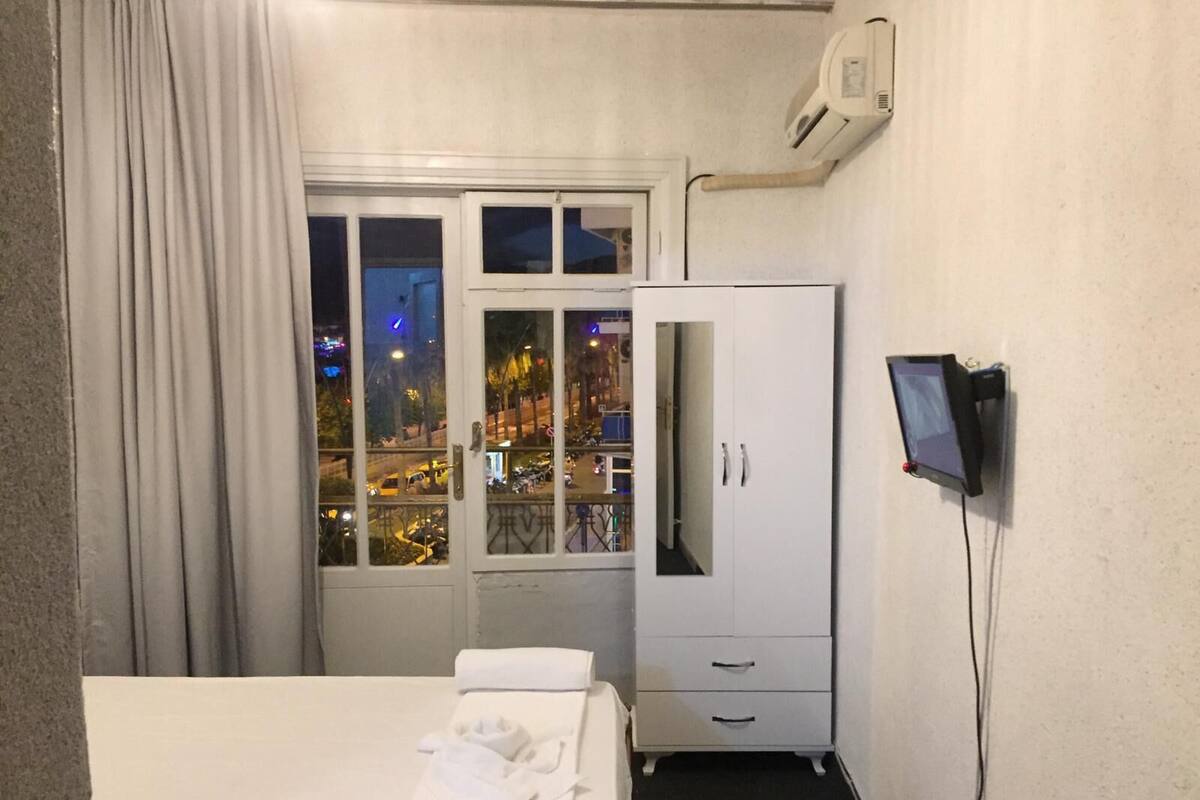 A hotel room with a bed, a wardrobe, a television, and a window with a view of the city at night.