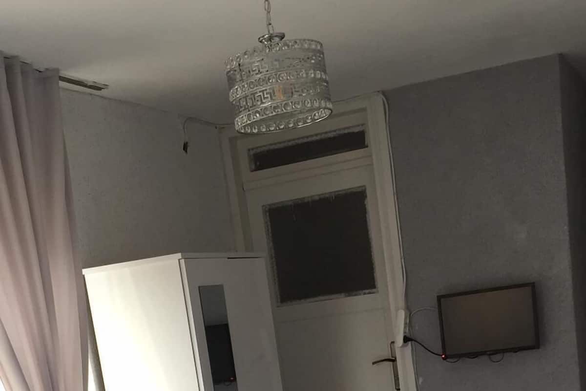 A hotel room with two beds, a wardrobe, a small table with a vase, and a television on the wall.